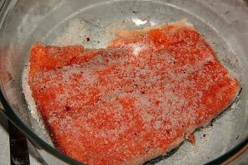 Вотрите половину соленого соединения в покрытую кожицей сторону лосося и выложите его на смесь укропа.